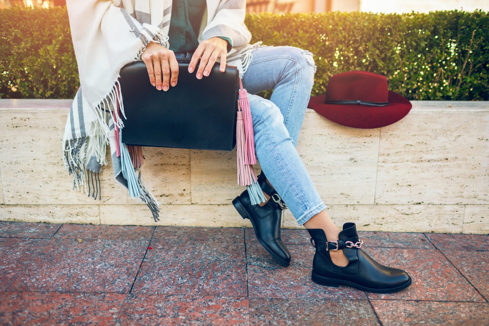 close up of woman legs wearing black leather boots, jeans, footwear spring trends, holding bag, hat, stylish accessories, shows details, street fashion style, sitting